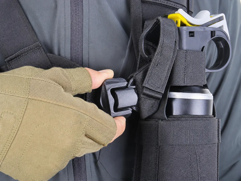 Close-up of the thumb-release retention buckle on the SOHAPI bear spray chest holster showing single-motion draw mechanism